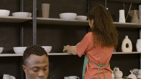 Young-Man-Packaging-Handicraft-Ceramics-With-Paper-In-The-Pottery-Shop-While-His-Female-Colleague-Working-On-Laptop-Computer-2