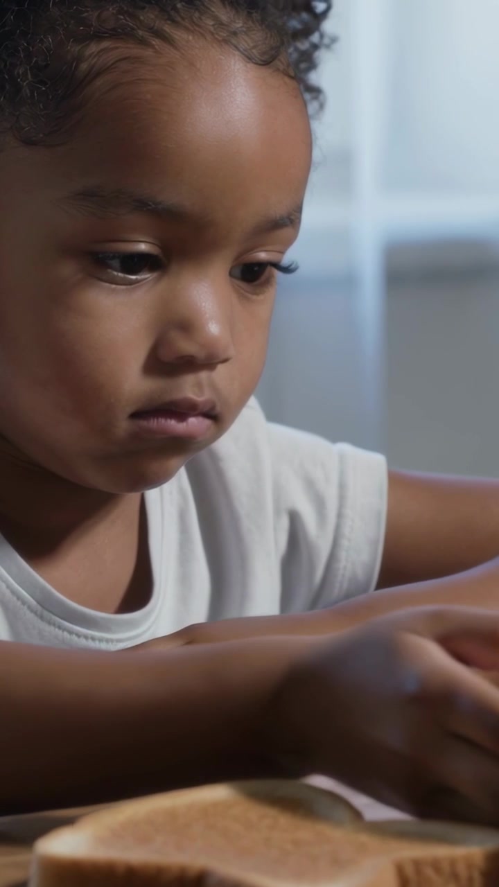 Video verticale: Bambino con maglietta bianca che nota i cereali, solleva la ciotola e ispeziona il latte al tavolo di casa.