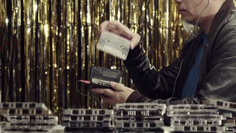 a man plays and checks copies of vintage cassettes with a cassette player and headphones - gold tinsel background