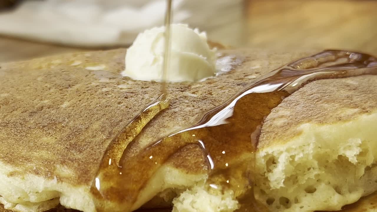 Maple syrup cascading over fluffy pancakes topped with rich butter, beautifully arranged on a rustic wooden table, capturing the essence of a delightful breakfast in Mexico, extreme close up