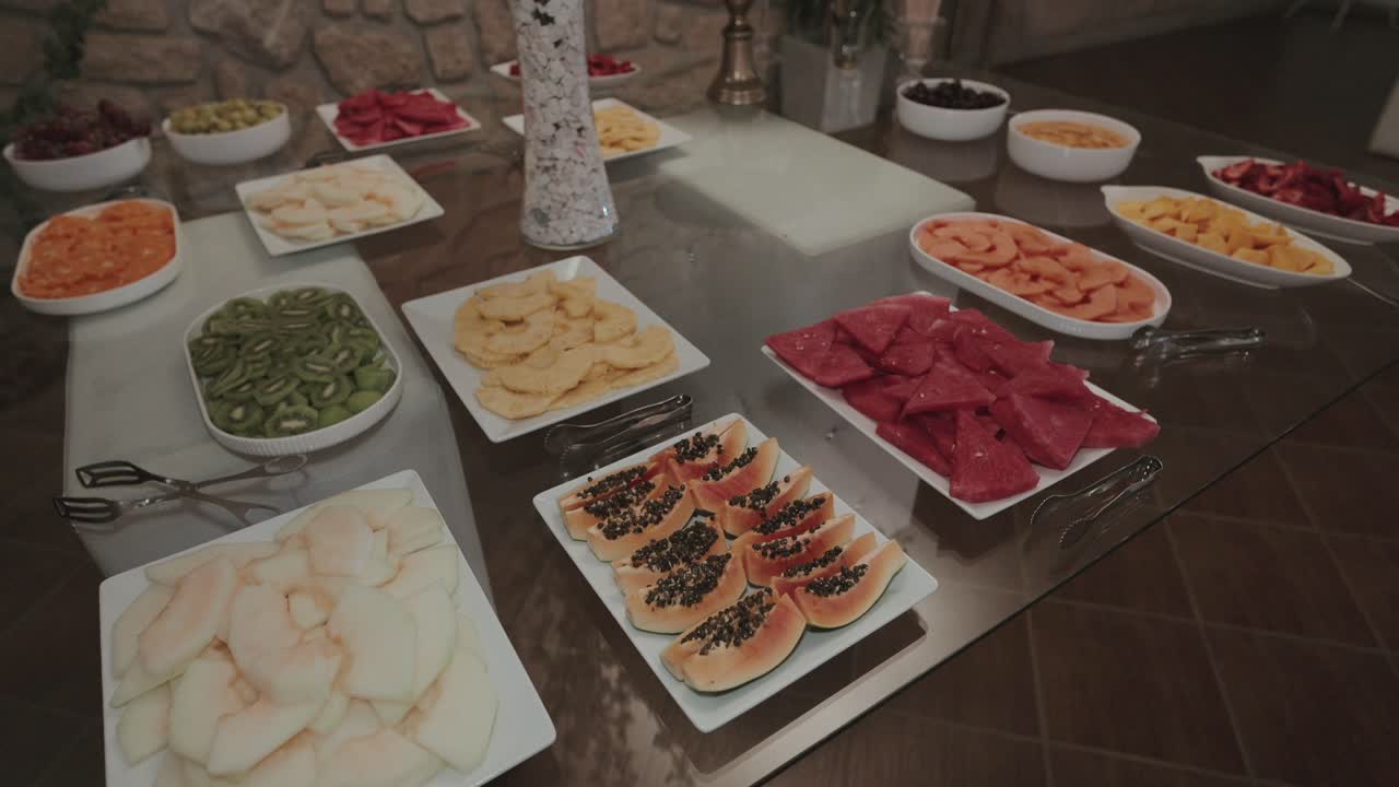 Variety of fresh sliced fruits arranged on a reflective wedding table with elegant tongs