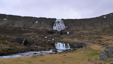 dynjandi waterfall cascading down rocky mountain slope into river below in iceland. majestic multi-tiered falls surrounded by rugged terrain and peaceful natural scenery