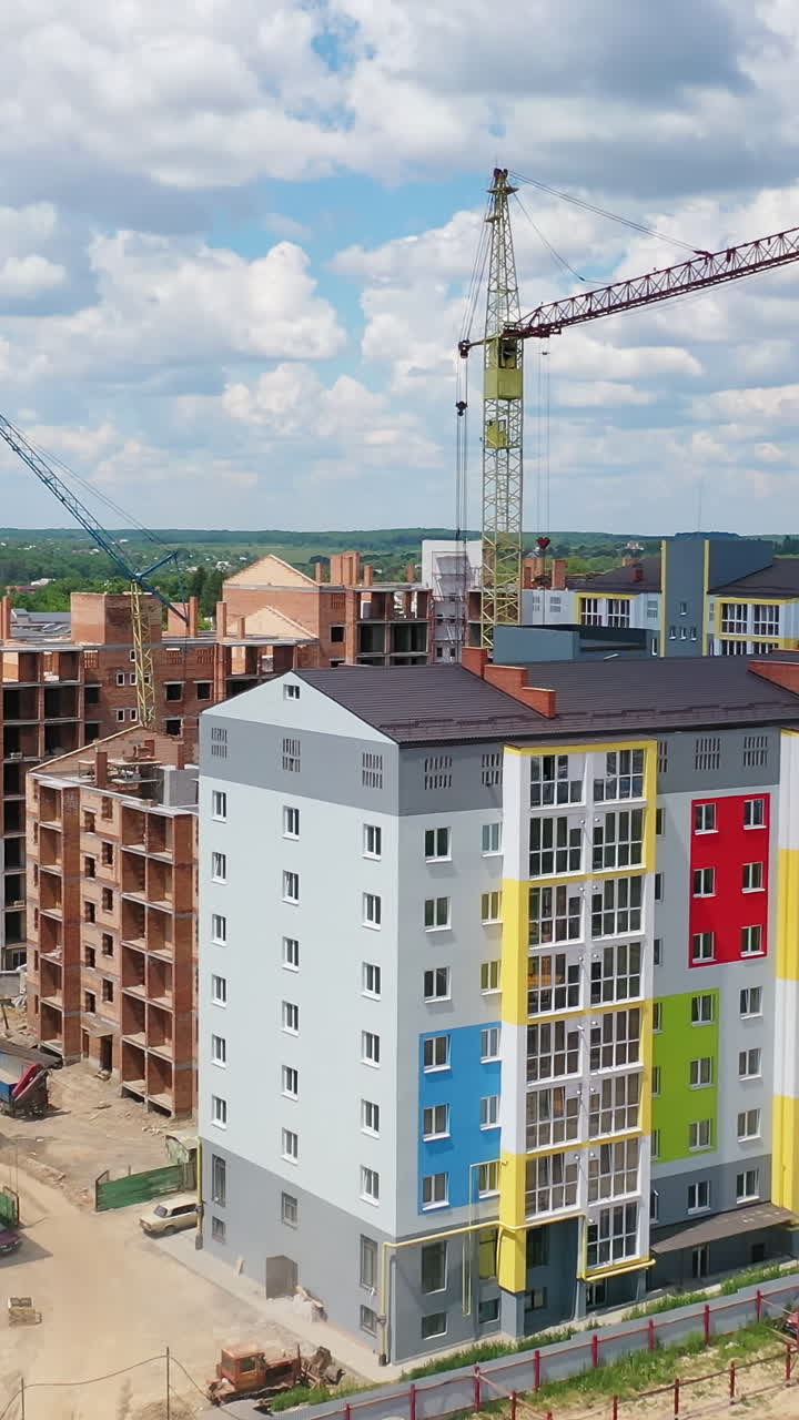 Colorful multi-storey building on a construction site. High rise buildings construction site. Big industrial tower crane with blue sky on background. Aerial drone view. City development. Vertical video