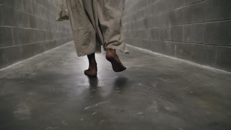 closeup of the feet of jesus wearing white robe walks in prison hallway in slow motion