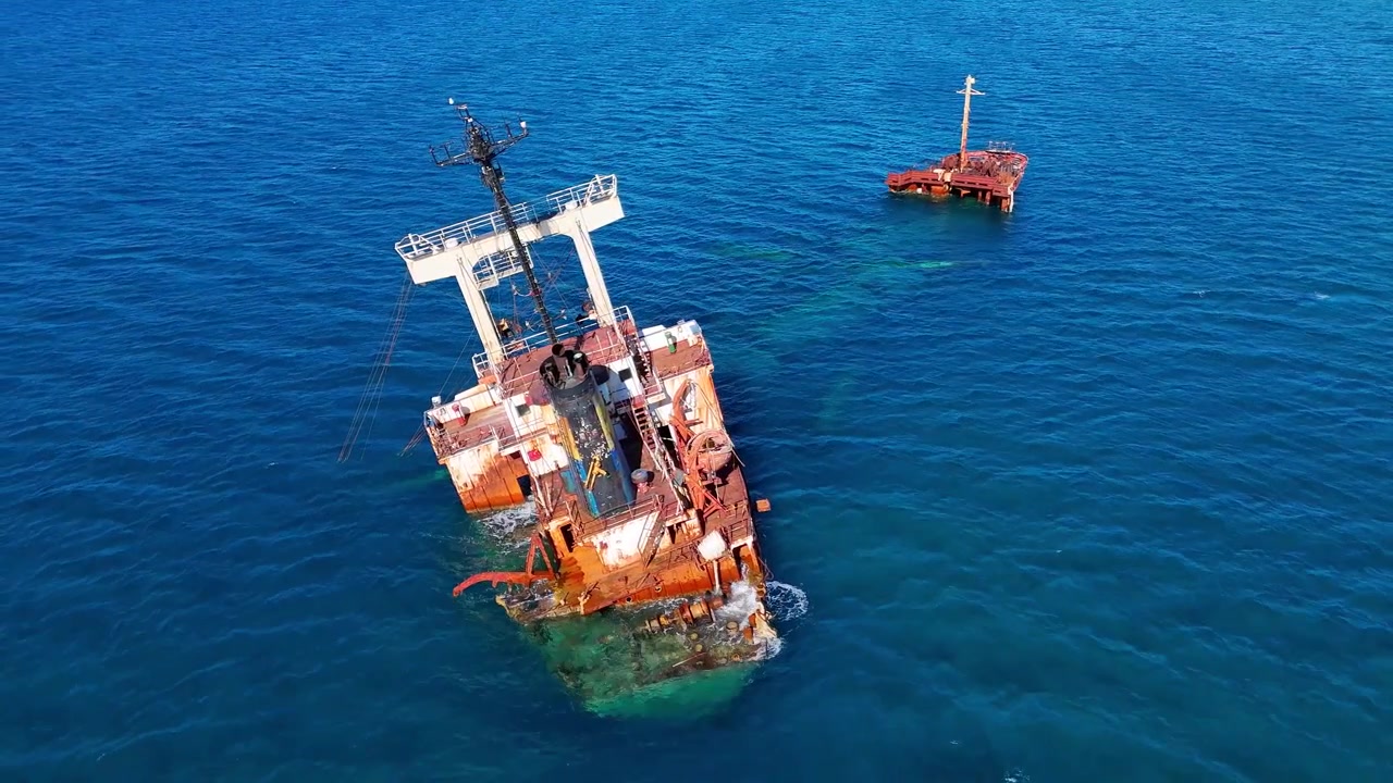 Manassa Rose M shipwreck lies offshore in Kissamos Bay near Drapanias, Kissamos, Chania, Crete, Greece, with its rusted cargo hull and broken stern visible above clear Mediterranean water drone static