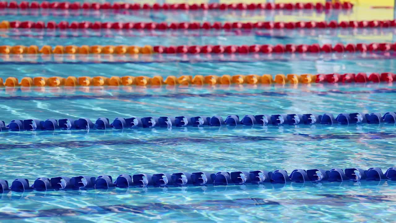 An athlete swims underwater in a competition pool, captured in slow motion with vibrant lane dividers and bright, even lighting from above