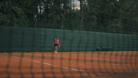 slow-motion side view of a young athlete trains the serve of the tennis ball. a teenage athlete is playing tennis on a court. an active girl is powerfully hitting a ball during sport practicing