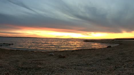 Leerer-Kieselabendstrand-Im-Sonnenuntergangszeitraffer-Mit-Wellen-Und-Wolken