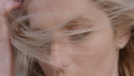 close up portrait beautiful young blonde woman running hand through hair blowing in wind looking sensual seductive female looking at camera slow motion