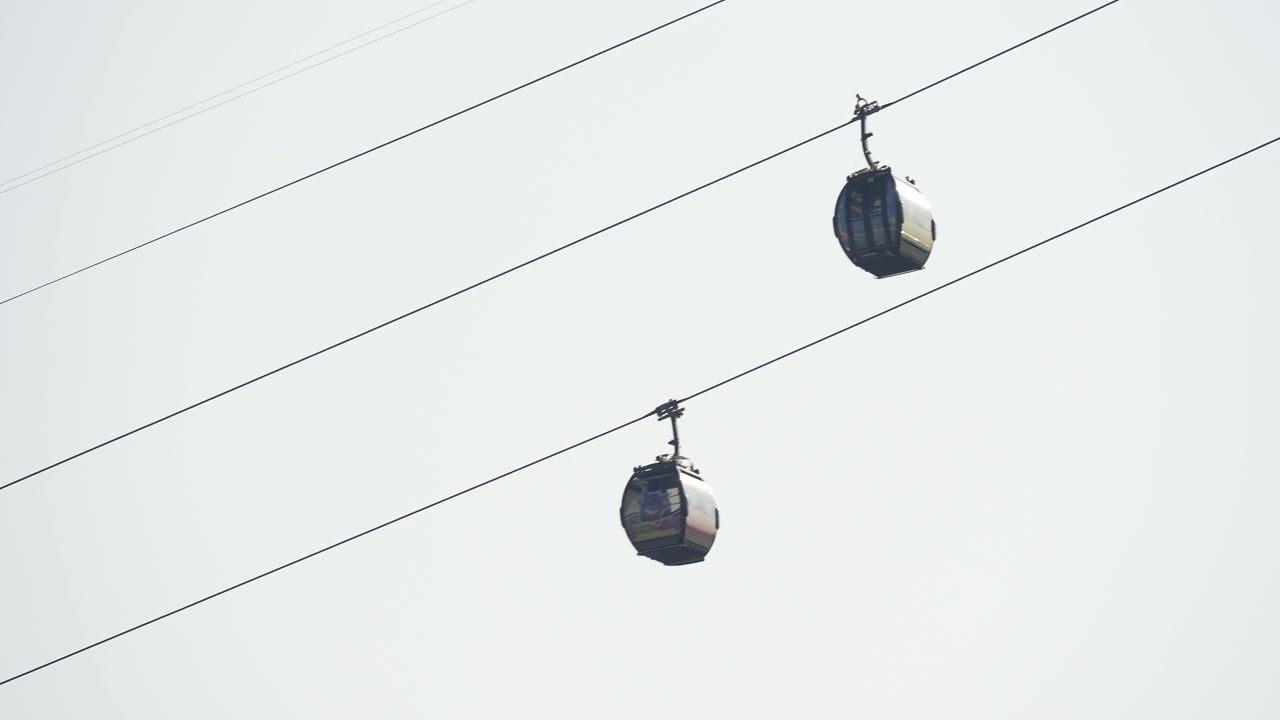 Singapore Cable Car cabins moving along high wire line against light sky.