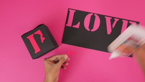 gluing pink letters on black paper to form word love in a-team font
