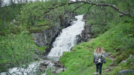 lady tourist trekking on lush mountain with cascading streams in background during daytime in norway. - backview