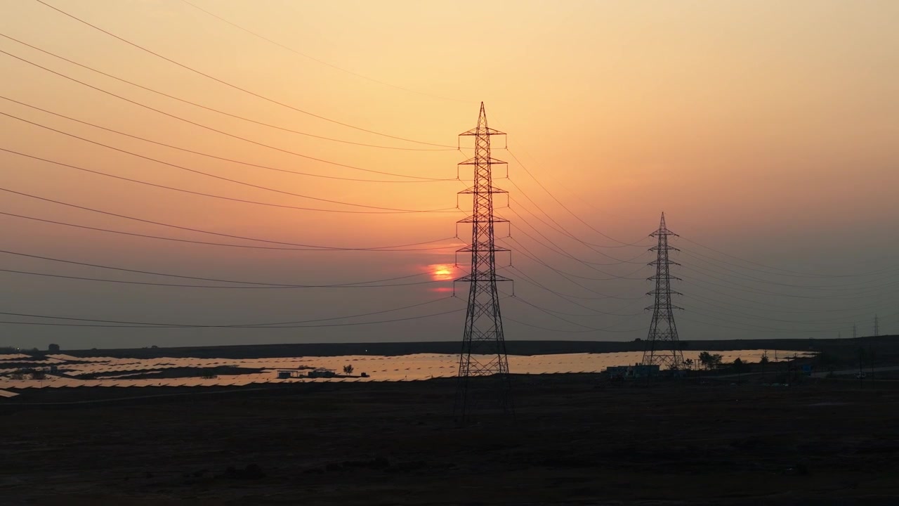 Drone tracking right over a solar power station at golden sunset with high-voltage towers and photovoltaic panels, showcasing renewable energy, clean electricity, and modern power infrastructure.