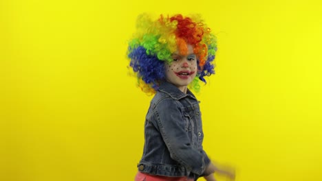 little child girl clown in rainbow wig making silly faces, fool around, smiling, dancing. halloween