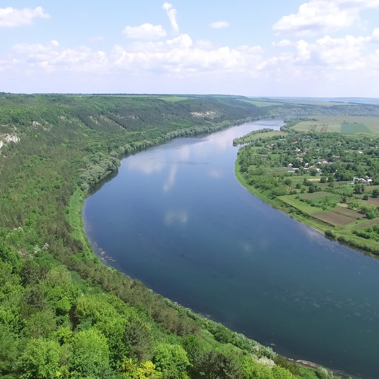View of the countryside with houses, fields and trees which are surrounded by wide river on the background of high rocks. Aerial view.