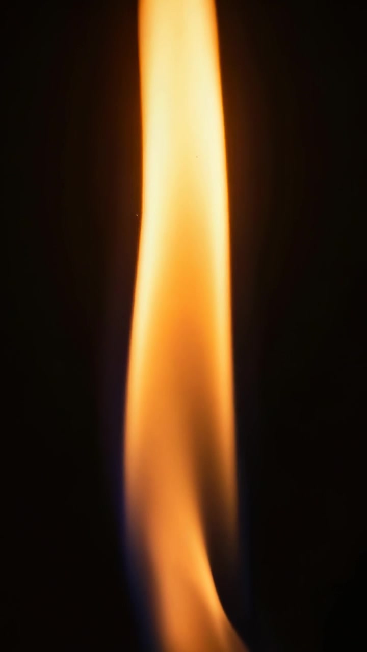 Vertical video: Flickering flame reacting to draft in dark space, with orange body and blue base
