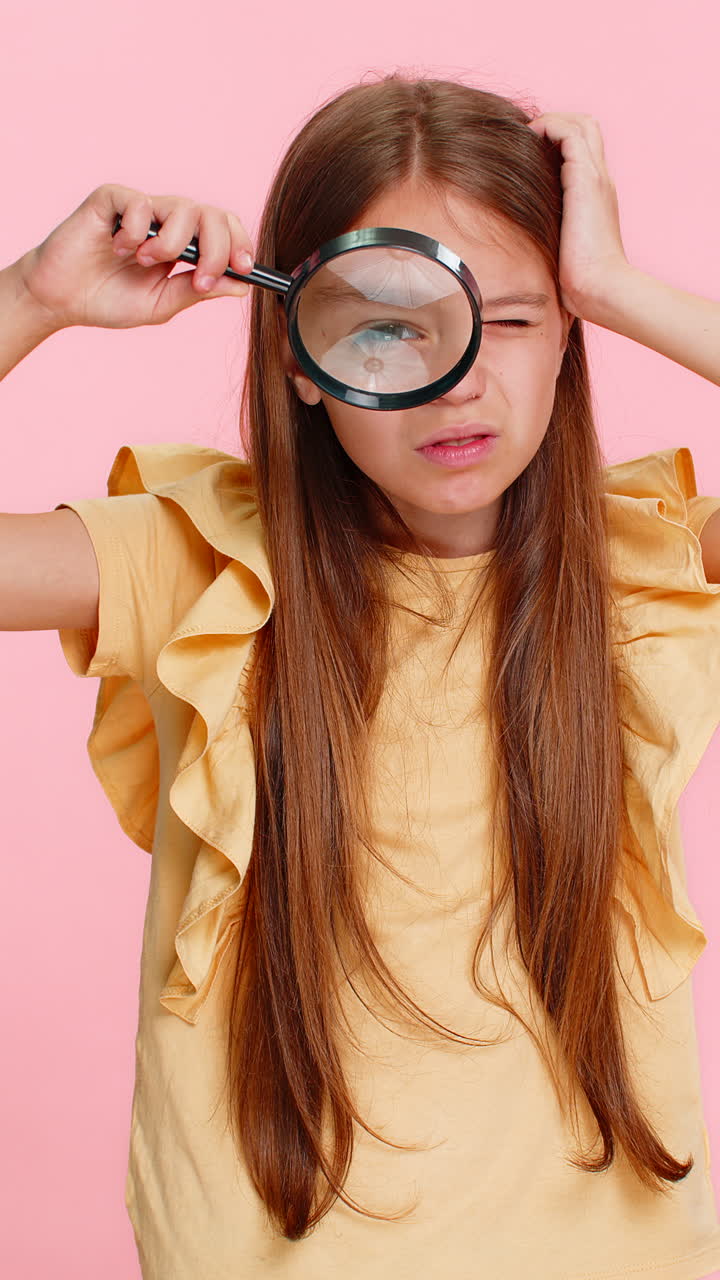 Child girl kid peeking through magnifying glass into camera while smiling with playful curiosity