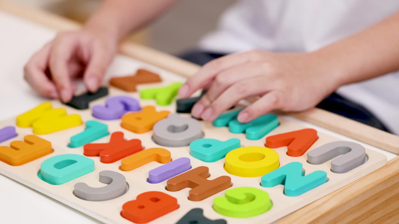 Young child’s hands organize multicolored wooden alphabet puzzle in bright, soft indoor lighting