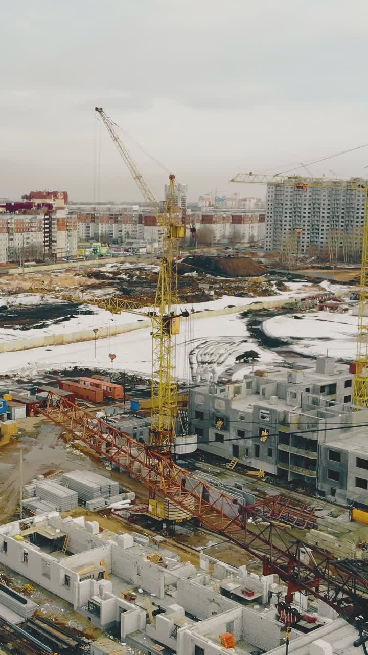 big construction cranes located in line on ongoing building against residential area and blue sky aerial view