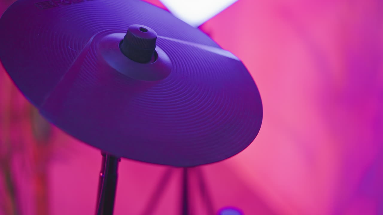 Close up of electronic cymbal pad struck by drummer using red stick under magenta studio lights highlighting grooves and motion blur conveying sharp percussion energy and surface texture