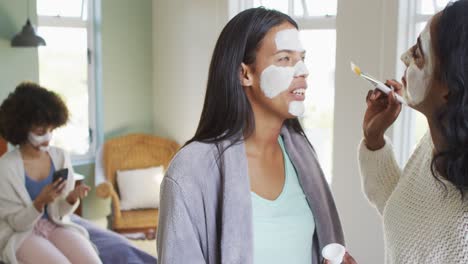 gelukkige diverse vrouwelijke vrienden die een schoonheidsmasker aanbrengen in de slaapkamer