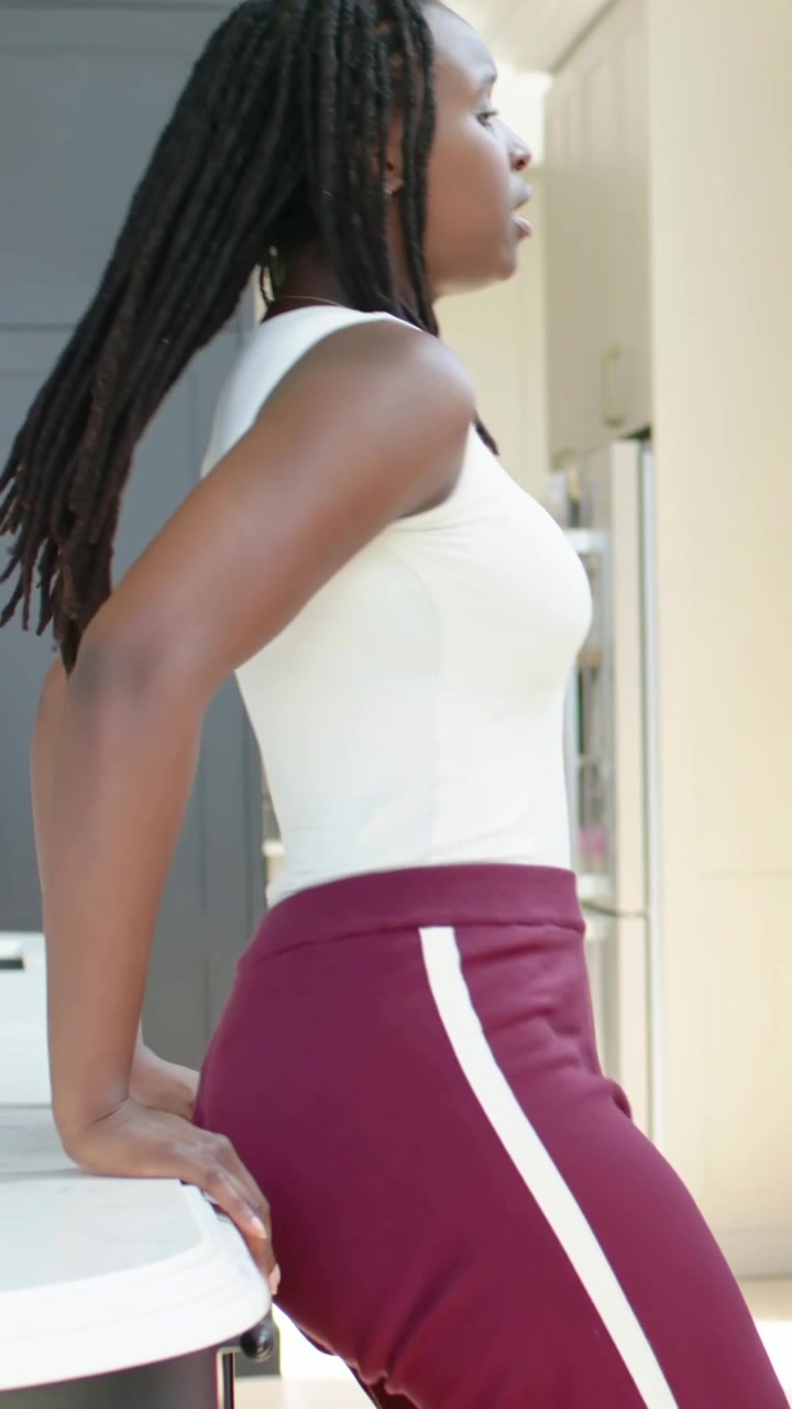 Video verticale: Donna con leggings color bordeaux che posa una tazza rosa sul bancone, si appoggia, si alza e se ne va.