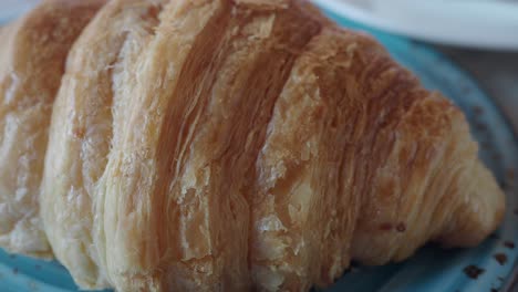 close-up of a golden, flaky croissant on a blue plate