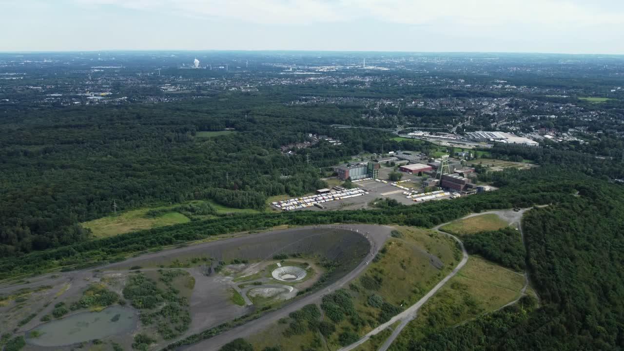 Aerial view of a landscape with a hill, forest, factory, and city