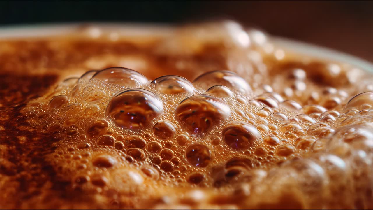 Gros plan captivant de mousse bouillonnante sur une surface riche, mettant en évidence la texture et les variations de couleur dans une boisson chaude aux tons marron et aux bulles pétillantes