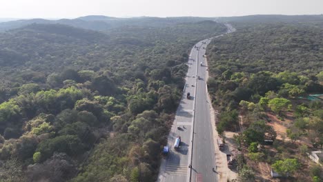 an aerial view of highway gracefully curves through a vast, dense green forest. vehicles move along the road, integrating infrastructure within a lush, natural environment under a clear sky