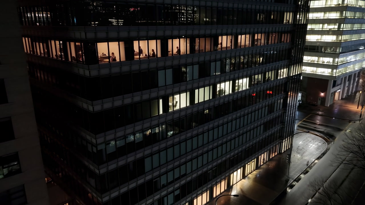 Night City Office Building Showing Silhouettes Latenight Workers And Security Staff In Lit Glass Tower,