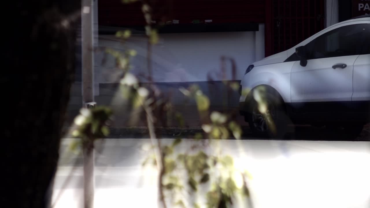 White car parked on a city street, seen through a window