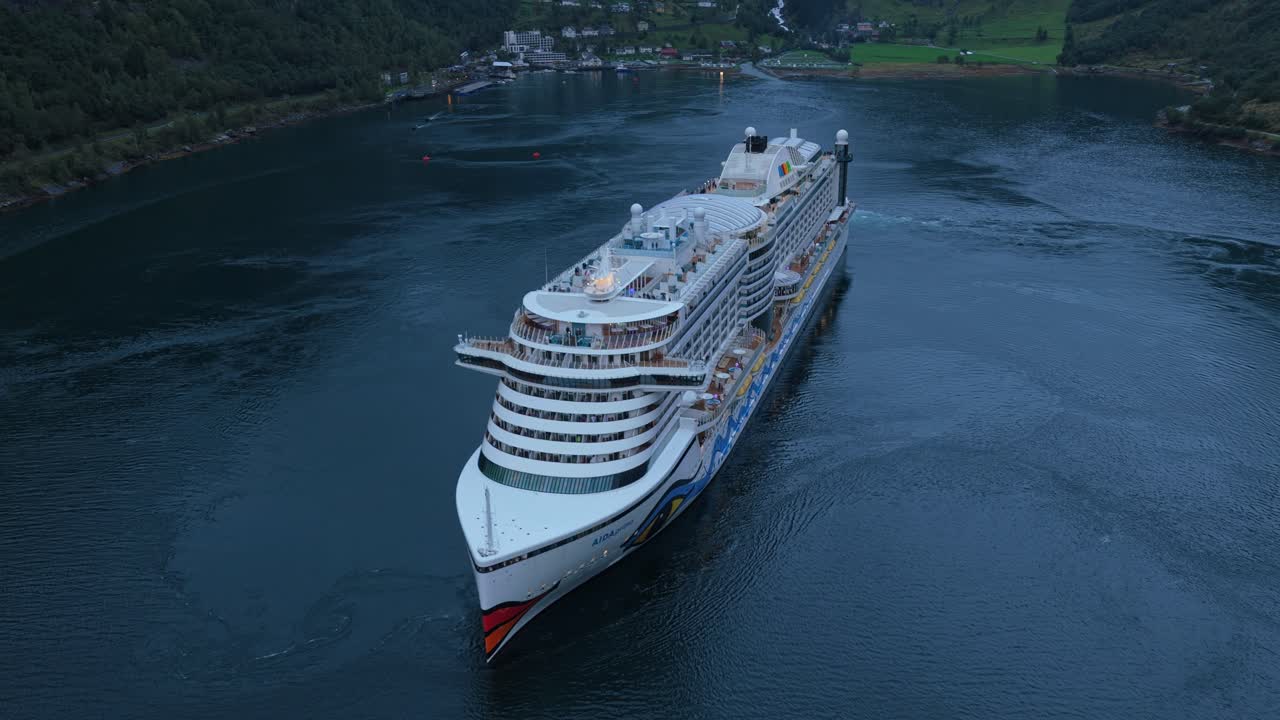 Luftfoto af krydstogtskib, der forlader Geiranger havn via den dybe fjord.