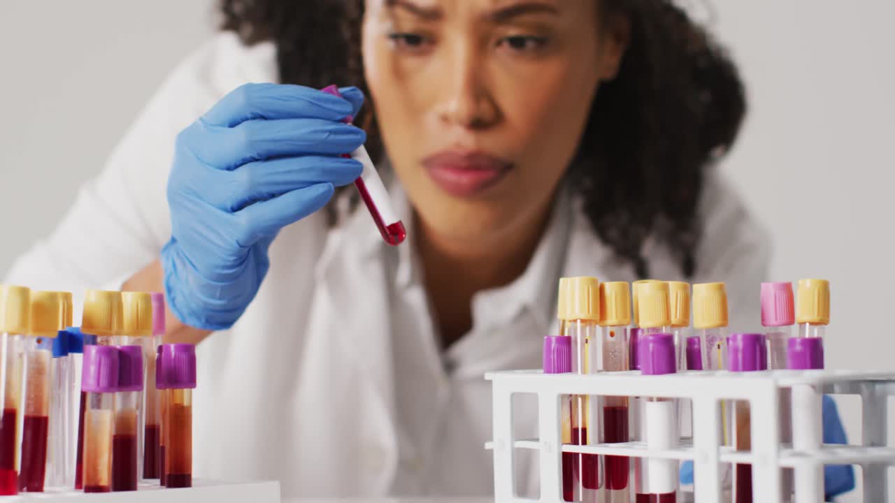 video de una doctora biracial sosteniendo un tubo de ensayo sobre un fondo azul