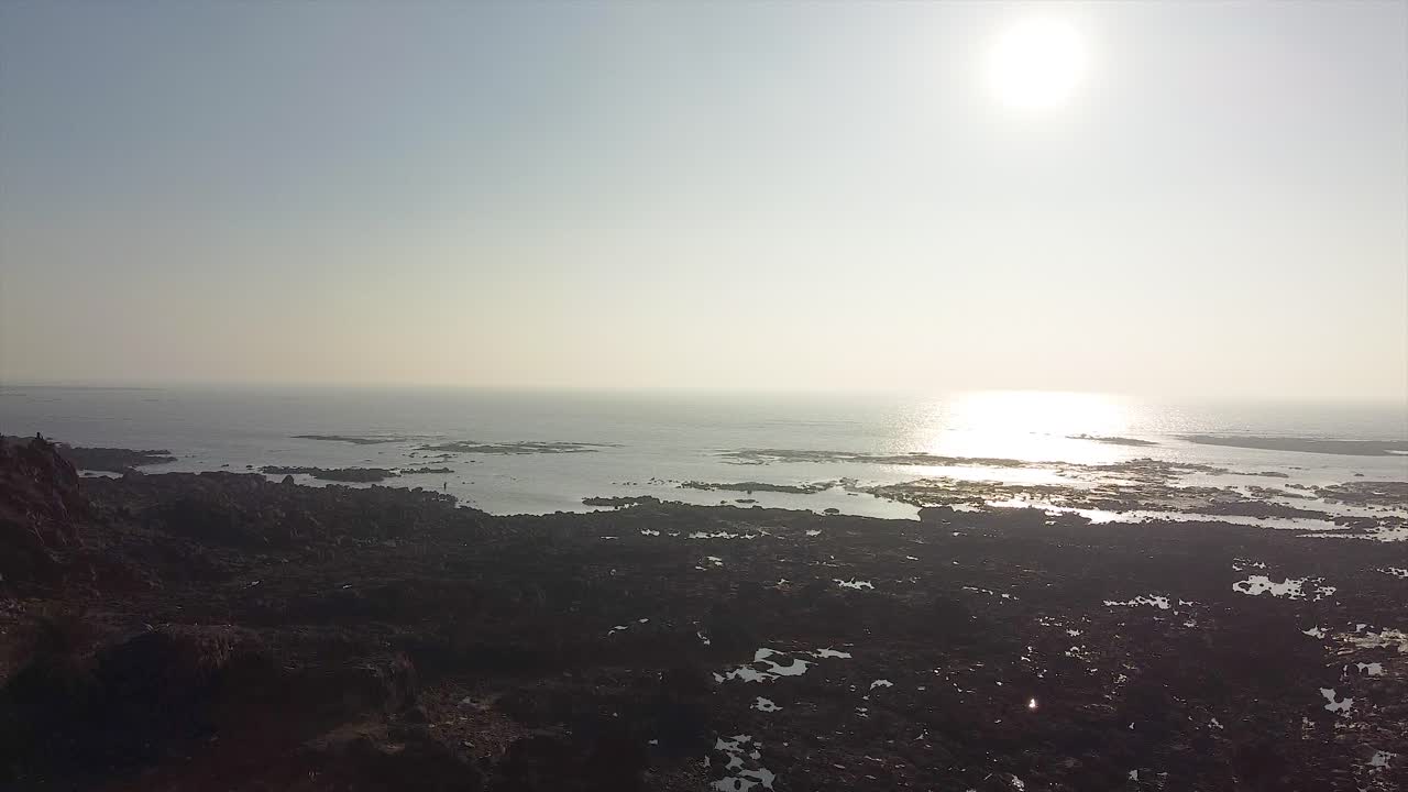 Arial view of a rocky coastline beach shore with a beautiful sunset view and reflection on ocean cinematic drone shot video background