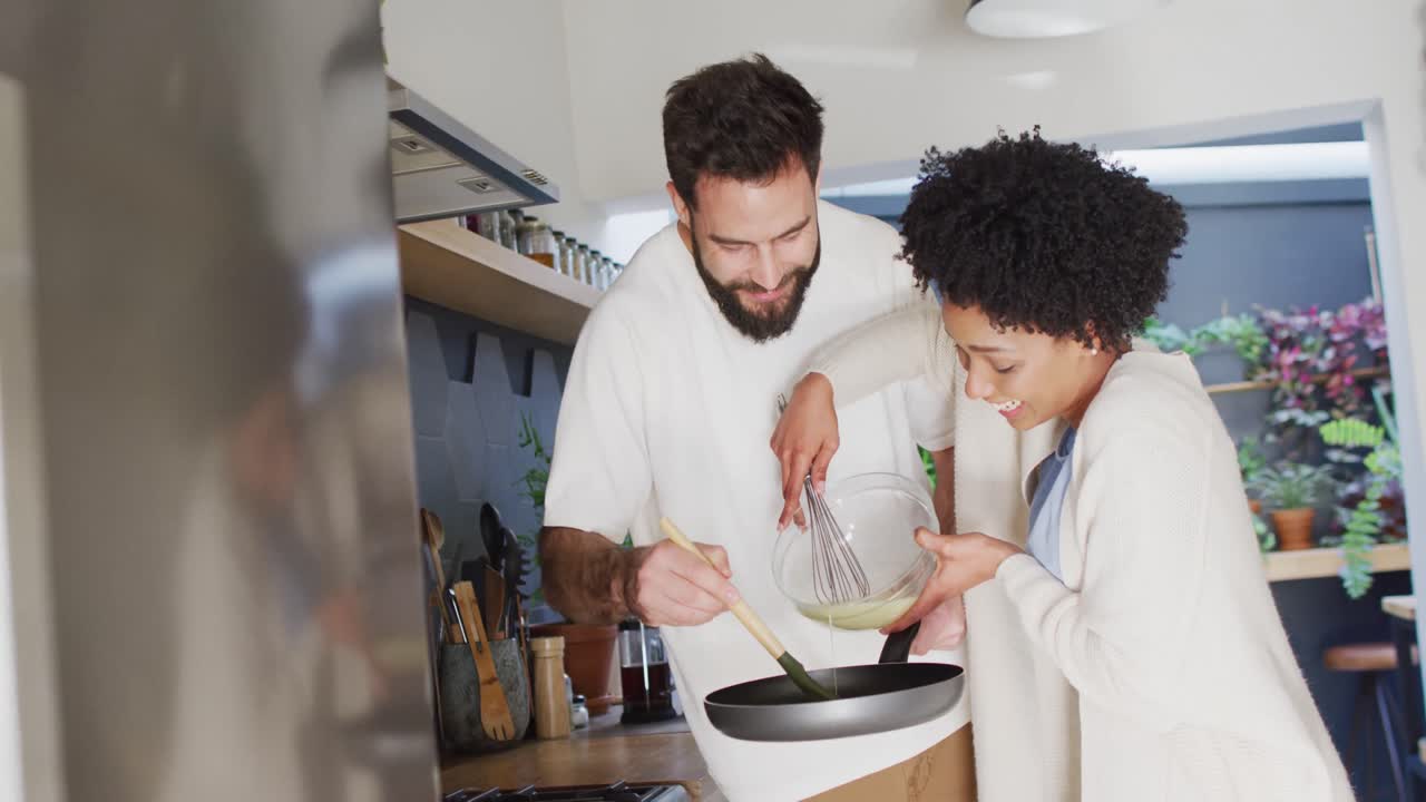 video de una feliz pareja diversa sonriendo y cocinando el desayuno en la cocina, con espacio para copiar