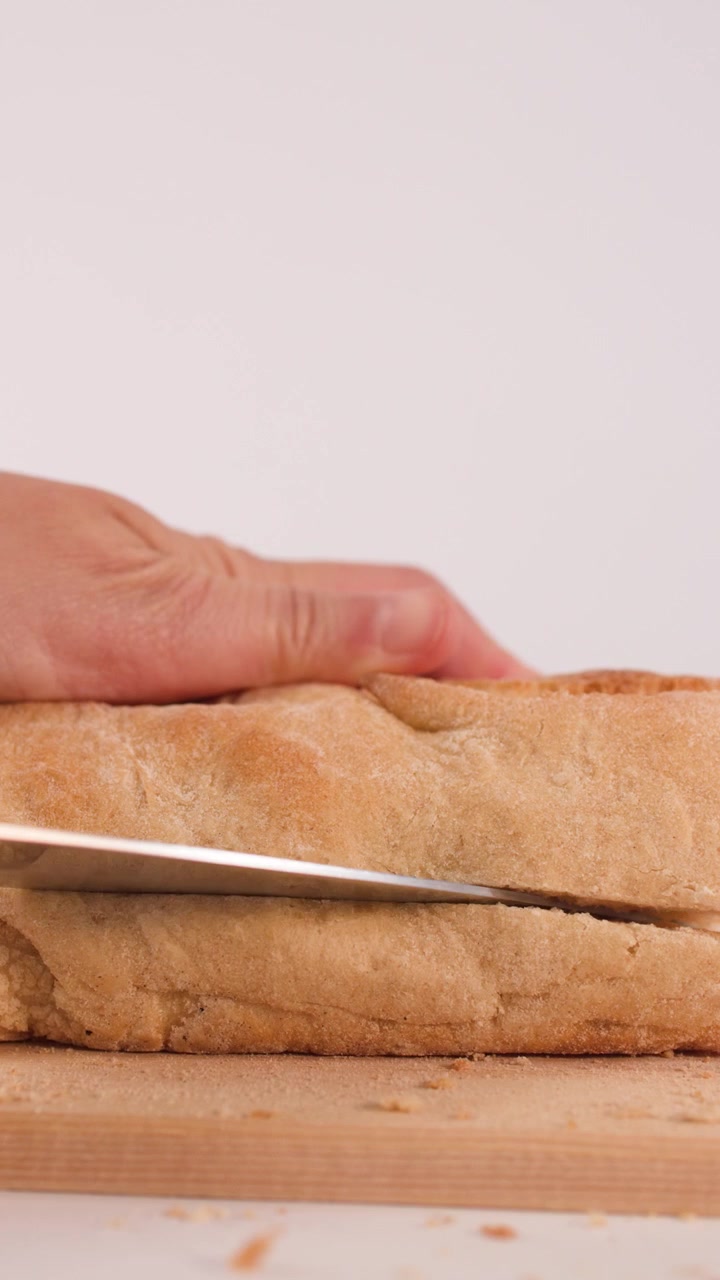 Primo piano di mani che usano un coltello per affettare orizzontalmente pane fresco a lievitazione naturale.