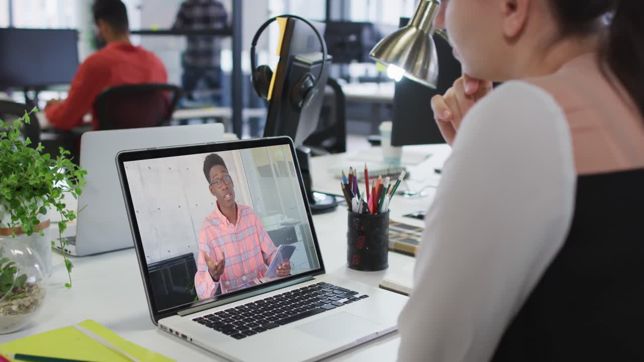Caucasian woman having a video call on laptop with male colleague at office