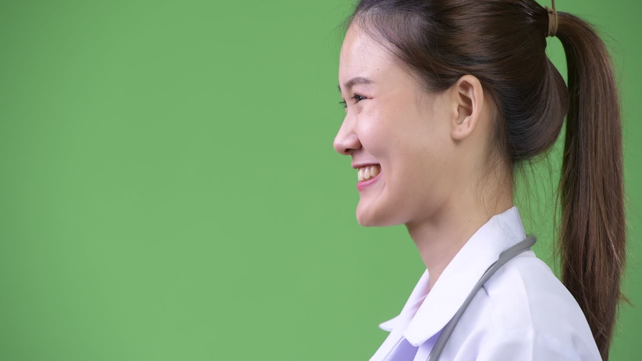 Profile view of young happy beautiful Asian woman doctor smiling