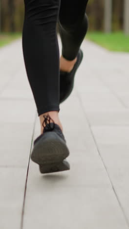 close-up leg view of runner wearing black sneakers running on a paved track through park, blurred background of green grass, highlighting athletic movement and jogging activity