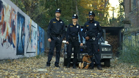 Retrato-De-Los-Policías-De-Razas-Mixtas,-Hombres-Y-Mujeres,-Parados-Al-Aire-Libre-Con-Un-Perro-Pastor-En-El-Coche-De-Policía