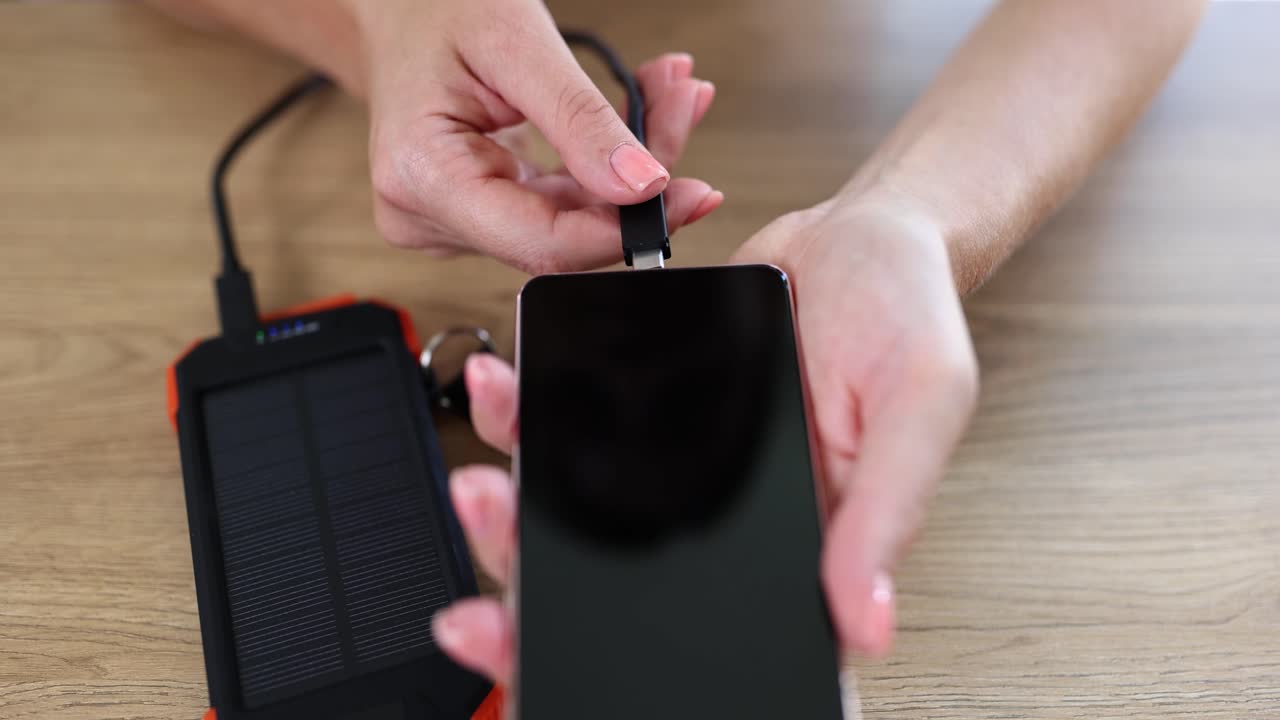 Person charging smartphone with solar power bank