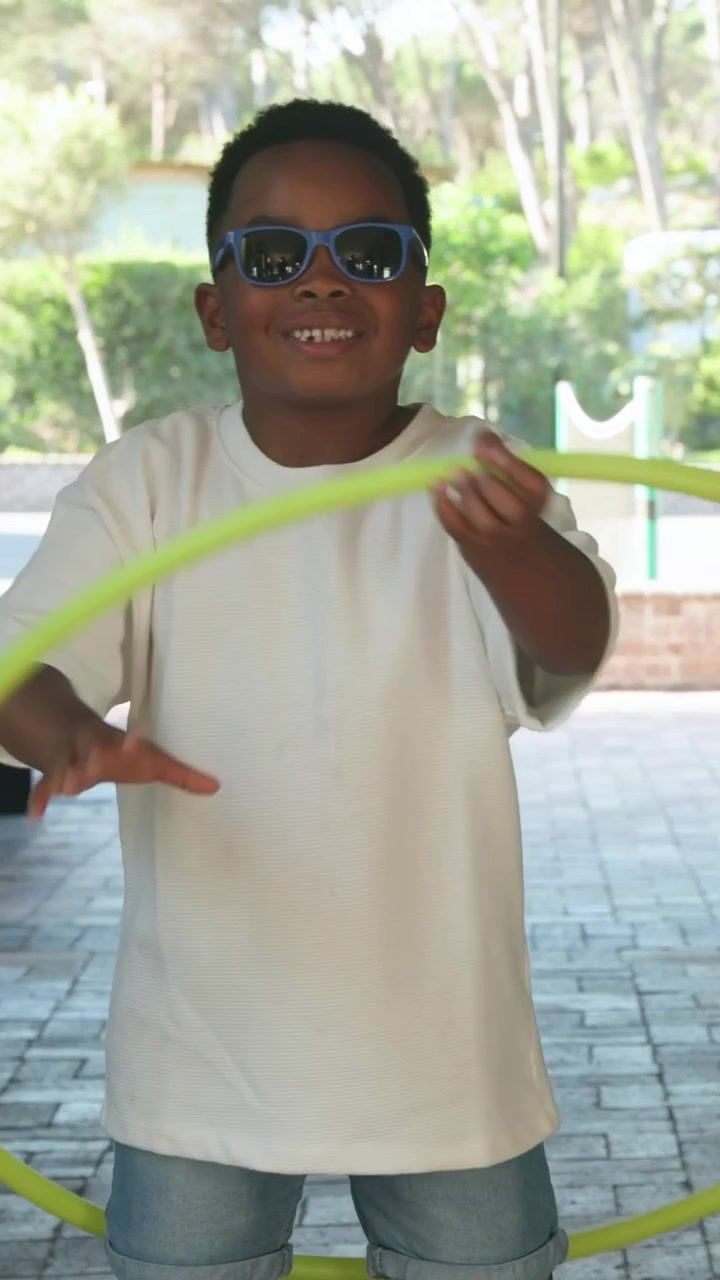 Vertical video: Starting with neon green hula hoop, boy spinning, practicing tricks at pavilion