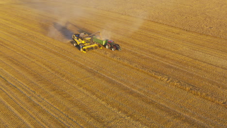 angled frontal view of combine harvester and tractor with long shadows behind under cloud of dust and smoke