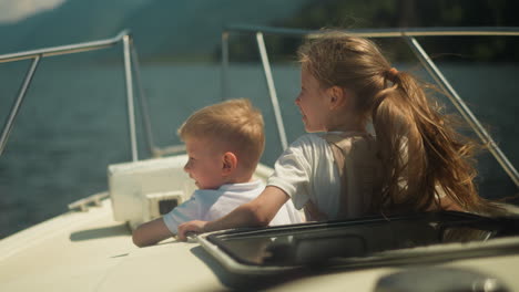 joyful little kids look around riding motorboat on windy day. happy brother and sister sail yacht in ocean bay on summer vacation. children life