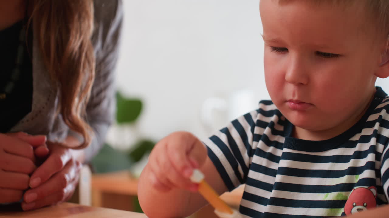 Autistic child with hearing aid guided by teacher during block arrangement task, close focus on thoughtful face, striped shirt, supportive hands nearby, calm classroom setting