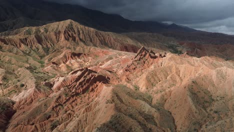 red rocky ridges of fairytale canyon in kyrgyzstan under dramatic cloudy skies