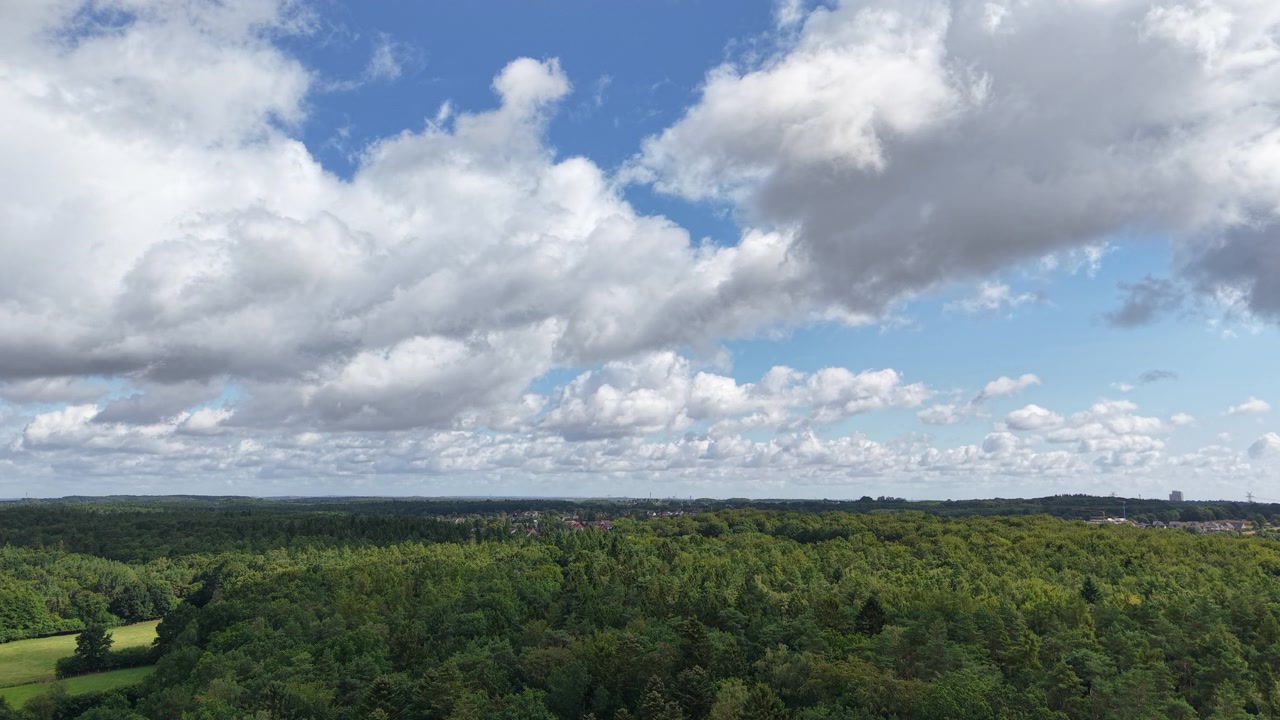 a view of dramatic clouds drifting over a vast green forest landscape beneath a blue sky, capturing the beauty of nature, changing weather, and peaceful wilderness from above.