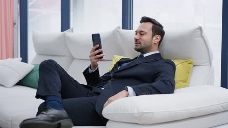 happy smiling middle-aged businessman in suit lying on the sofa looking at his phone