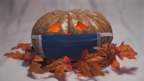 Halloween-pumpkin-with-a-face-mask-and-autumn-leaves